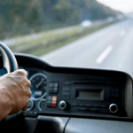 Hand on steering wheel of truck driving ahead